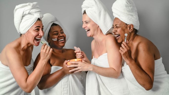 Vier Frauen in Handtüchern lachen und genießen gemeinsam eine Spa-Behandlung.