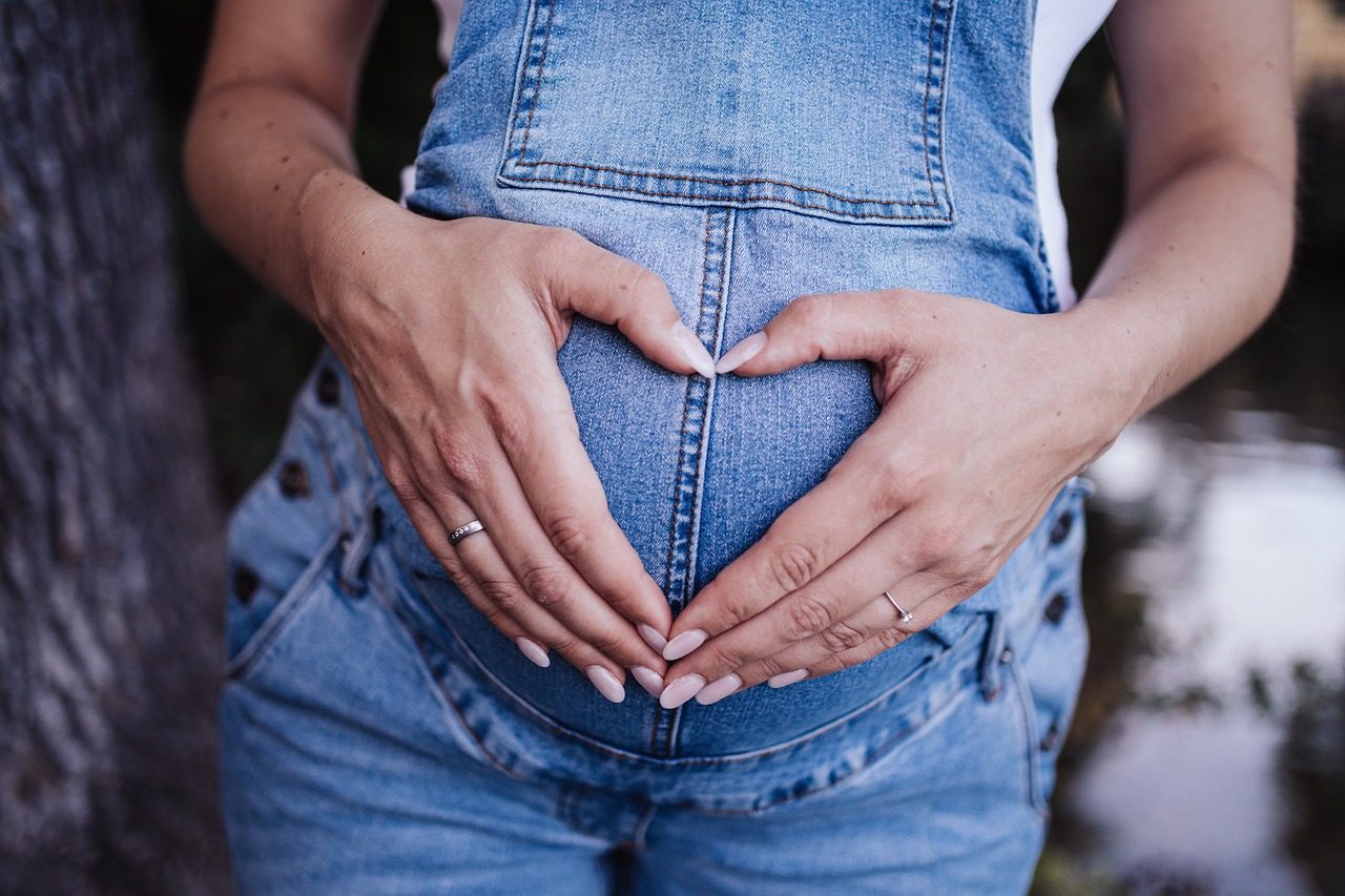 Frau formt mit ihren Händen ein Herz vor ihrem schwangeren Bauch