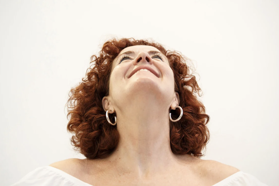 Frau mit roten lockigen Haaren lächelt und schaut nach oben.