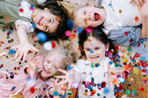 Vier fröhliche Kinder streuen Konfetti und lachen zusammen.