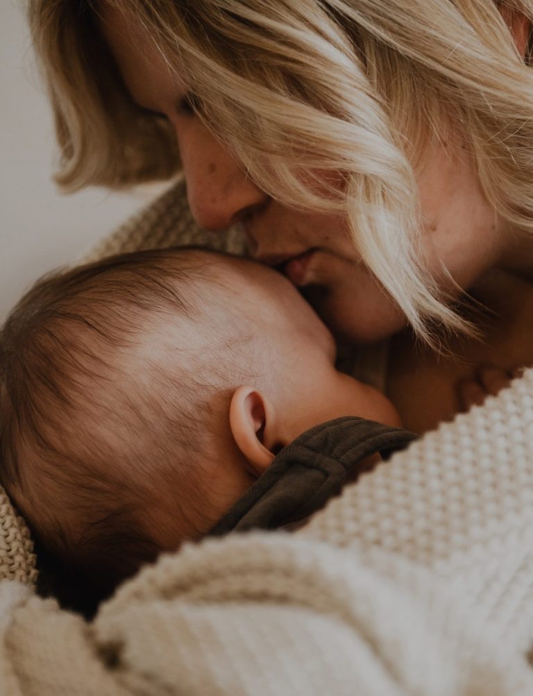 Frau küsst ihr Baby liebevoll auf die Stirn, während sie es eng umschlungen im Arm hält