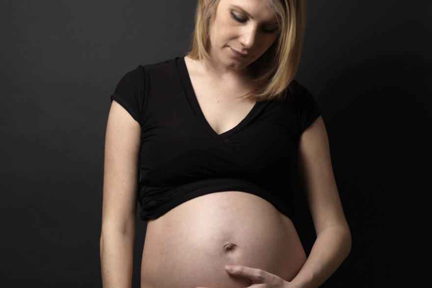 Wenn Sorgen wachsen - Umgang mit Sorgen in der Schwangerschaft Schwangere Frau in schwarzem Oberteil betrachtet ihren Bauch.