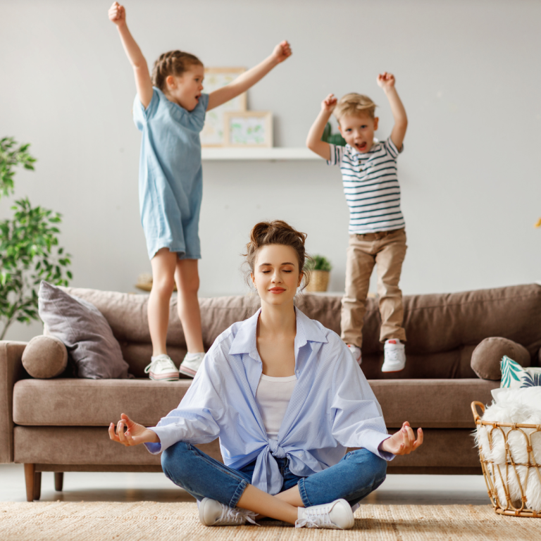 Mutter meditiert vor ihren beiden wild auf dem Sofa springenden Kindern