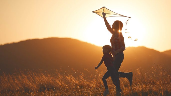 Eine Mutter spielt mit ihrem Kind und hält einen Drachen im Sonnenuntergang.