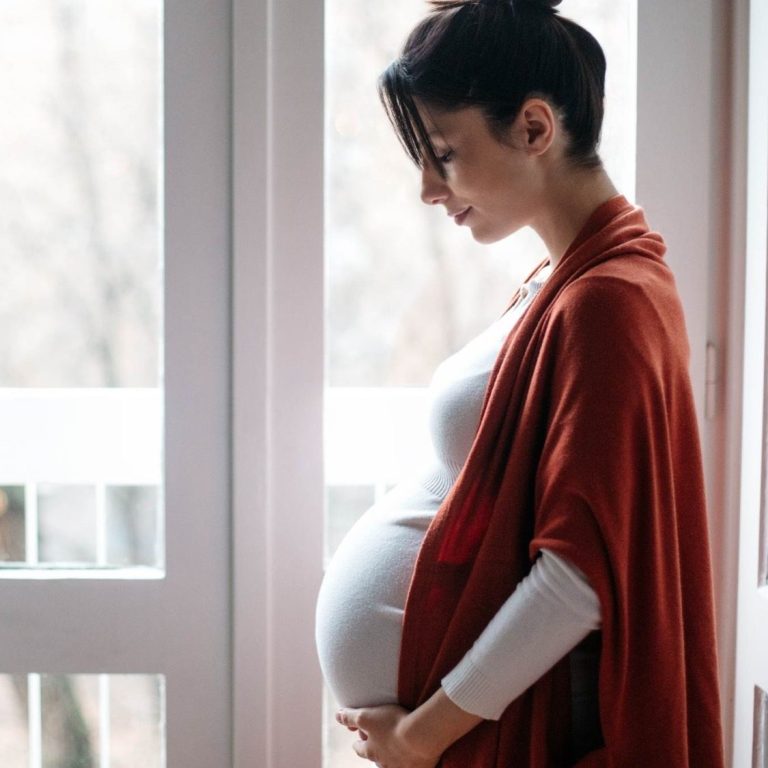 Schwangere Frau in einem roten Schal, die ihren Bauch liebevoll hält.