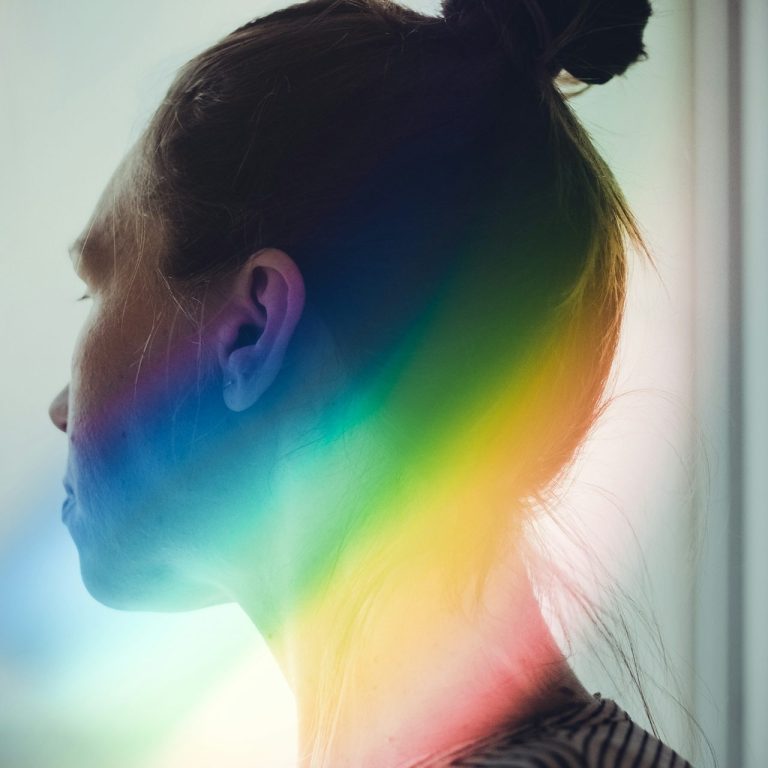 Profilansicht einer Person mit einem Dutt, umgeben von einer Regenbogen-Lichtreflexion.