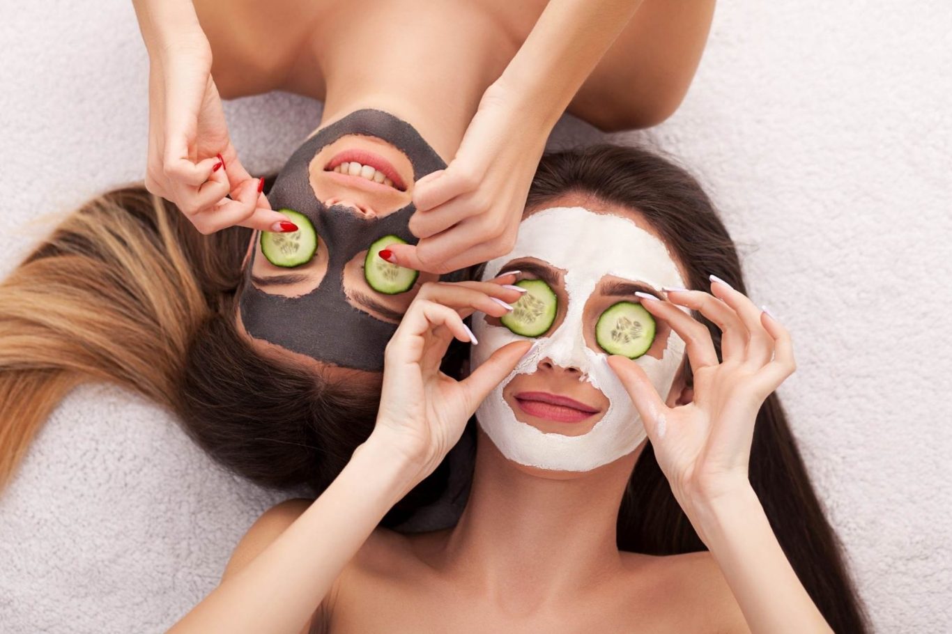 Zwei Frauen mit Gesichtsmasken und Gurkenscheiben auf den Augen entspannen gemeinsam.