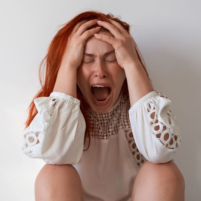 Frau tränenverschmierter Schminke hält ein Blatt mit einem lächelnden Gesicht vor sich.