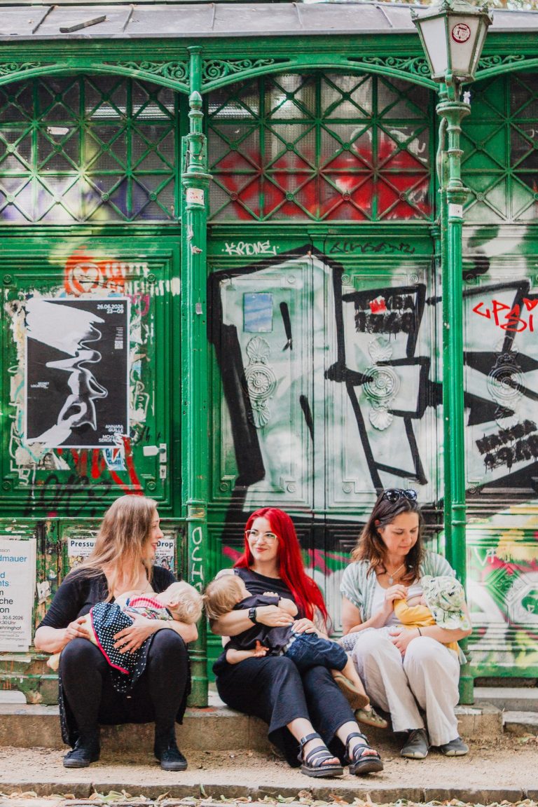 Foto: Una Oge, StudioUna Drei Frauen sitzen vor einer bunten Graffiti-Wand und stillen jeweils ihre Babys.