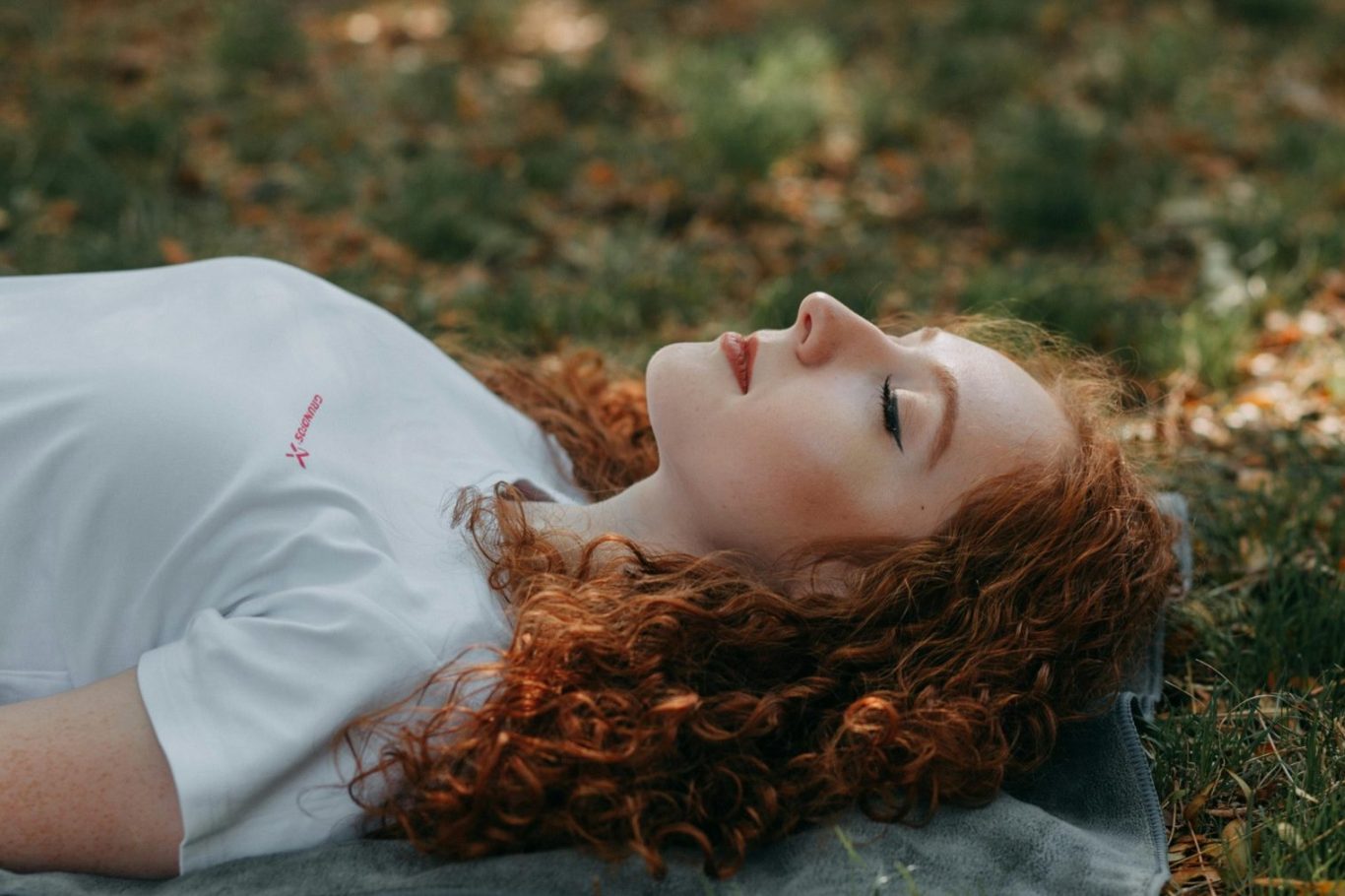 Mental Detox - Regulation des Mama-Nervensystems Eine Person mit roten, lockigen Haaren liegt entspannt auf dem Gras.