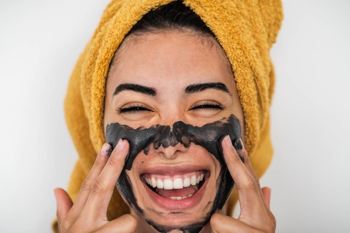 Lächelnde Frau trägt eine schwarze Gesichtsmaske und hat ein Handtuch im Haar.