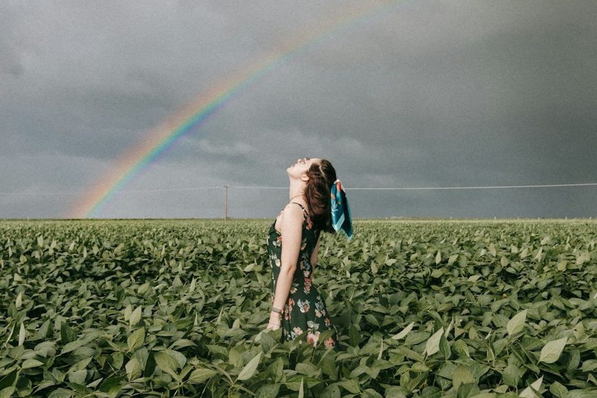 Regenbogen der Hoffnung - Wieder schwanger nach Verlust Frau in einem Feld, die sich entspannt, während ein Regenbogen den Himmel schmückt.