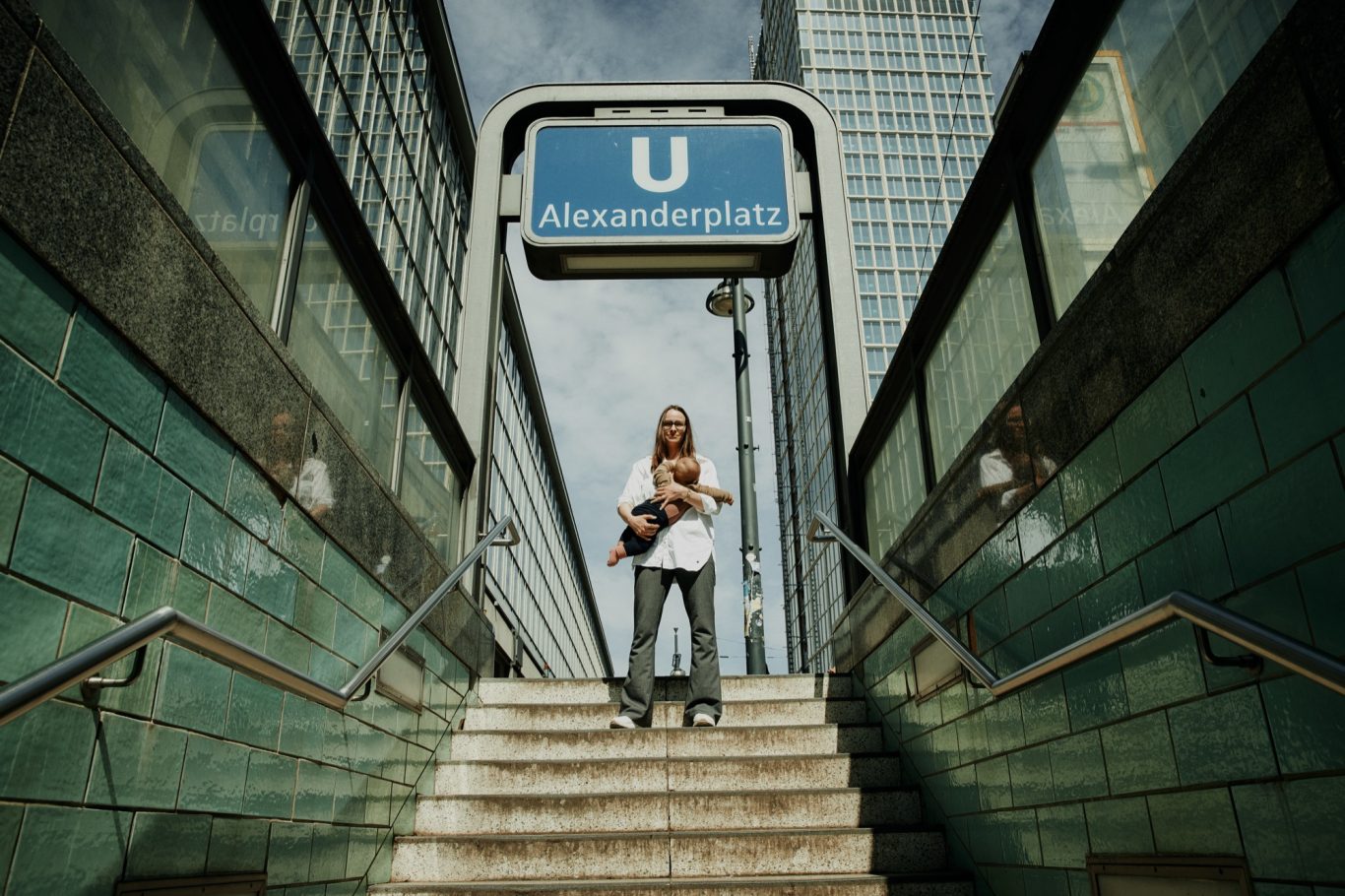Foto: Lovis Trummer Photography Frau stillt ihr Baby am Aufgang zur U-Bahn-Station Alexanderplatz, Stufen zur Haltestelle sichtbar.