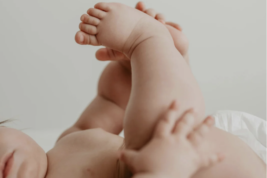 Babymassage & Babyyoga Ein kleines Baby mit sichtbaren Füßen und Händen auf einem weißen Untergrund.