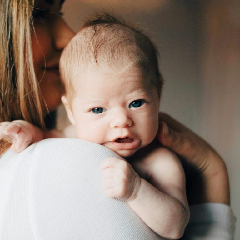 Ein Baby wird von einer Person gehalten und schaut neugierig in die Kamera.