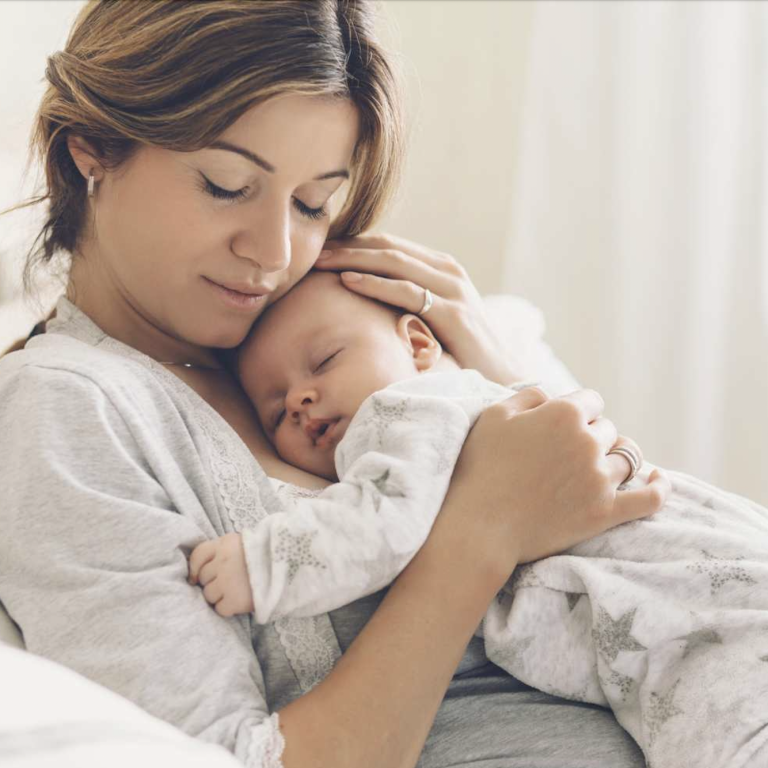 Eine Mutter hält ihr schlafendes Baby in den Armen, beide wirken entspannt und geborgen.