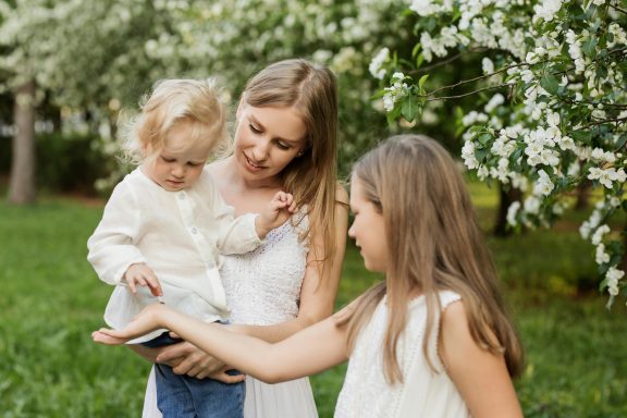 Mutter mit zwei Töchtern in einem blühenden Garten, die gemeinsam Blumen sammeln und bewundern