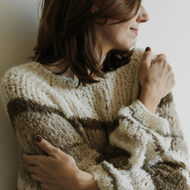 Frau in einem gestreiften, gemütlichen Pullover, mit den Armen um sich geschlungen.